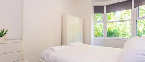 A bedroom with a bed, a dresser, a mirror, and a window with a view of greenery.