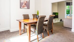 A dining area with a wooden table and four chairs, a framed artwork on the wall, and a television in the background.
