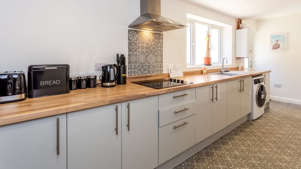 A modern kitchen with a bread maker, coffee maker, and kettle on the counter, a built-in stove, and a washing machine.