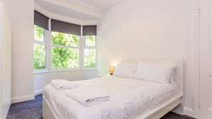 A bedroom with a bed, a window with a view of greenery, and a nightstand with a lamp.