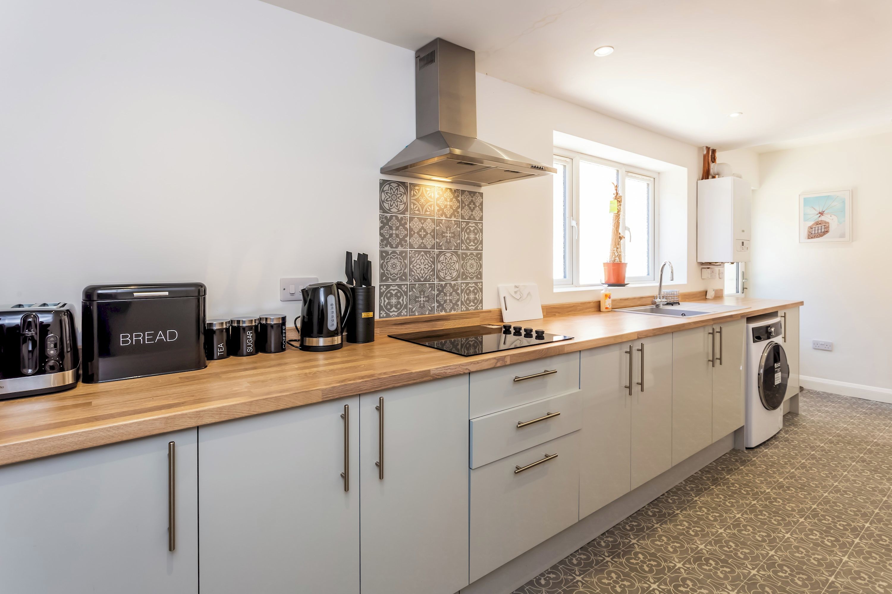 A modern kitchen with a built-in toaster, kettle, and coffee maker, a stainless steel range hood, and a window with a view of the outdoors.