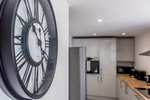 A modern kitchen with a large wall clock, built-in appliances, and a wooden countertop.