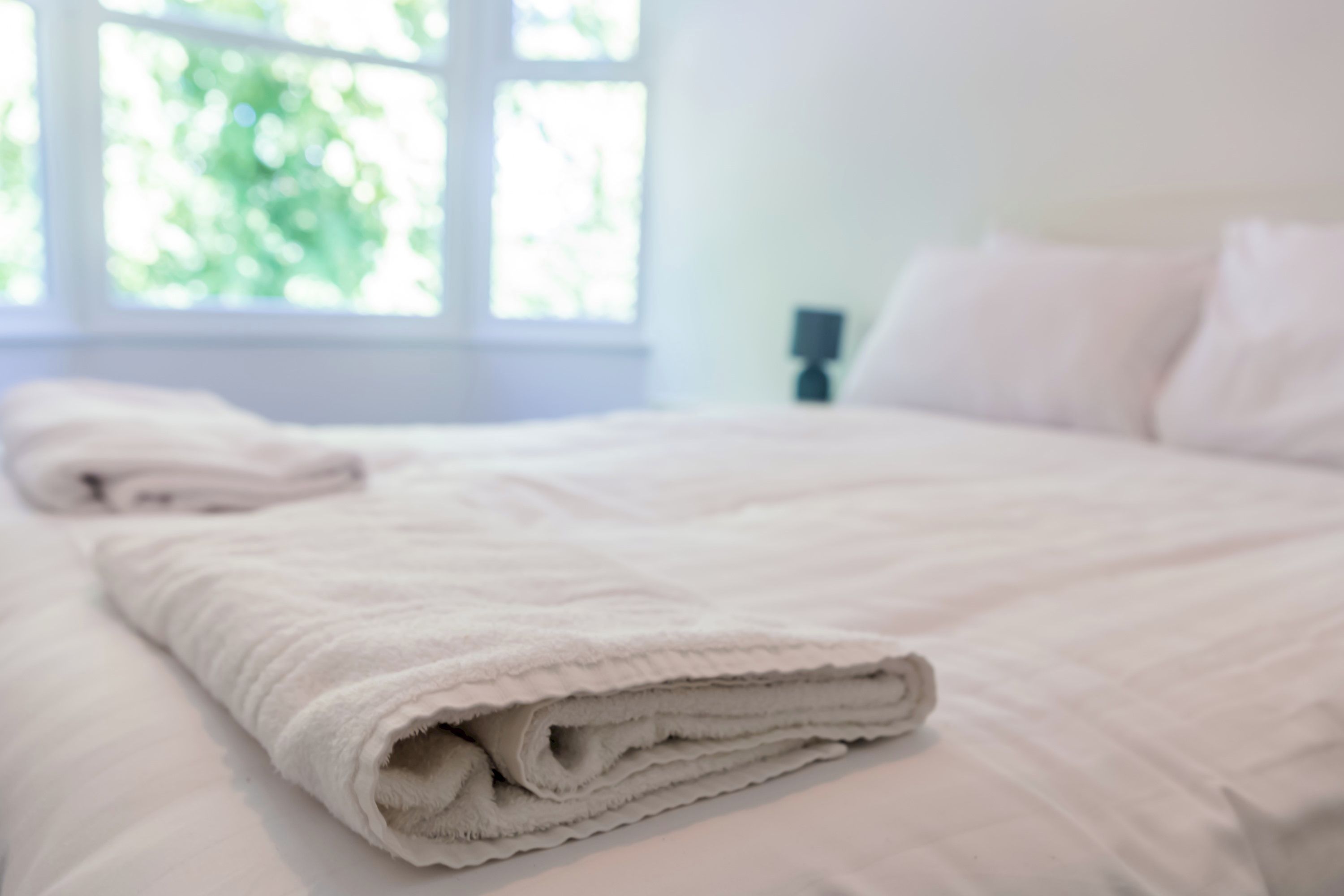 A neatly made bed with a folded white blanket in a room with a window.
