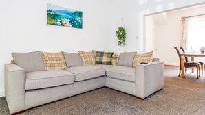 A modern living room with a grey sectional sofa, a painting of a landscape, and a hanging plant.