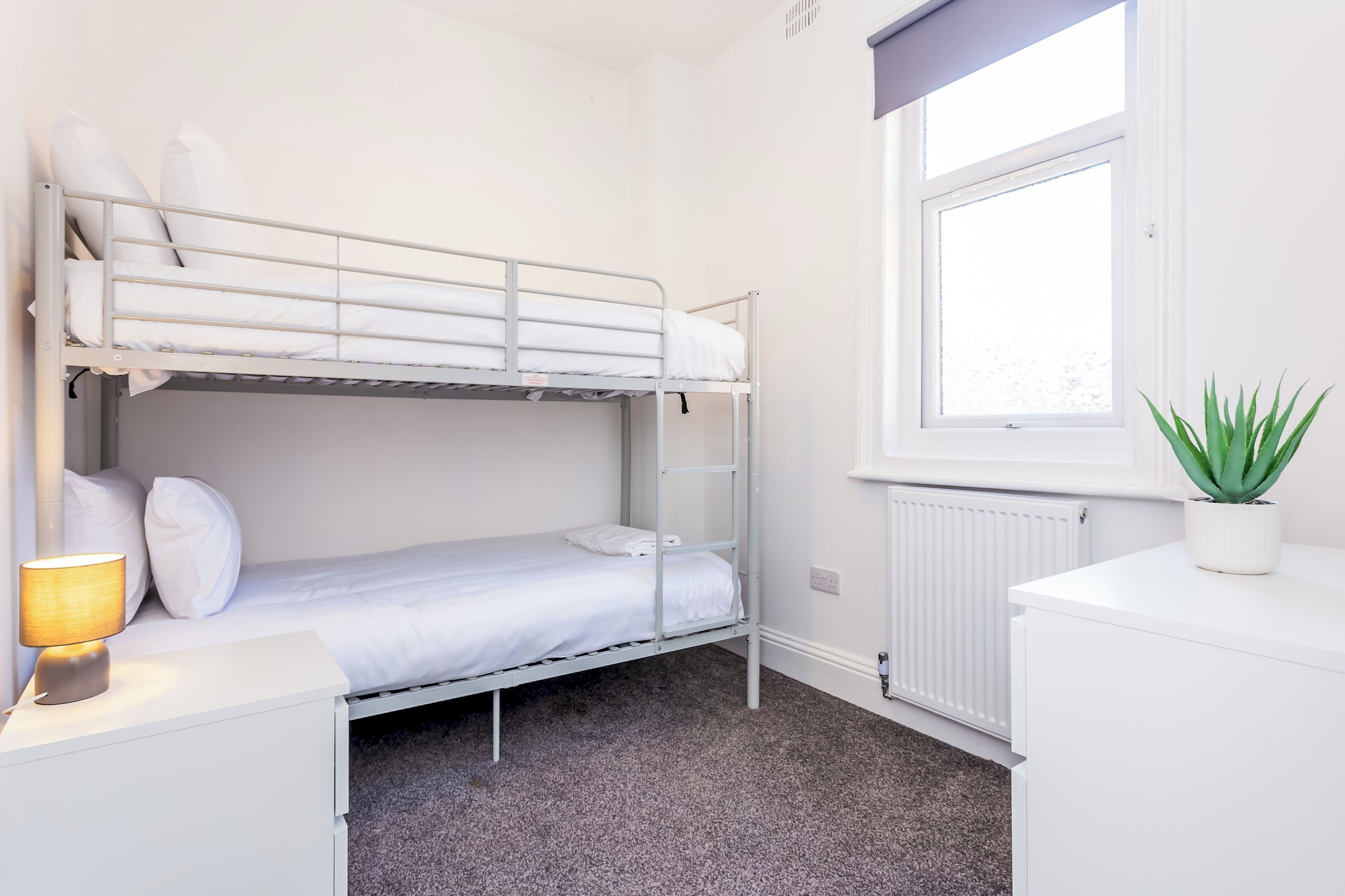 Ein Schlafraum mit Etagenbetten, einem Fenster, einem Heizkörper, einem Schreibtisch und einer Lampe.