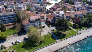 An aerial view of a residential area with a waterfront, featuring multi-story buildings, a paved walkway, and parked cars. - Blue Lake Apartments (Ohrid)