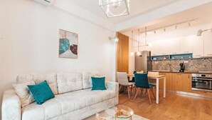 A modern living room with a sofa, a glass coffee table, and a dining area with chairs. - Blue Lake Apartments (Ohrid)