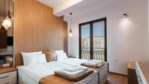 A modern bedroom with a large bed, wooden paneling, and a view of the city through a window. - Blue Lake Apartments (Ohrid)