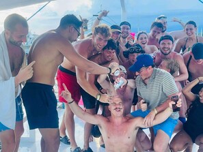A group of people on a boat, some holding drinks and others interacting closely.