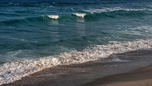 A beach with waves approaching the shore, a clear sky, and distant landforms. - Apto c Varanda Garagem e Vista das Montanhas (Angra dos Reis)