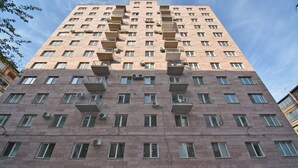 A high-rise building with multiple balconies, air conditioning units, and a clear sky.