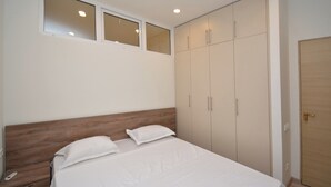 A bedroom with a wooden headboard, a bed with white bedding, a wardrobe with multiple doors, and a window above the bed.