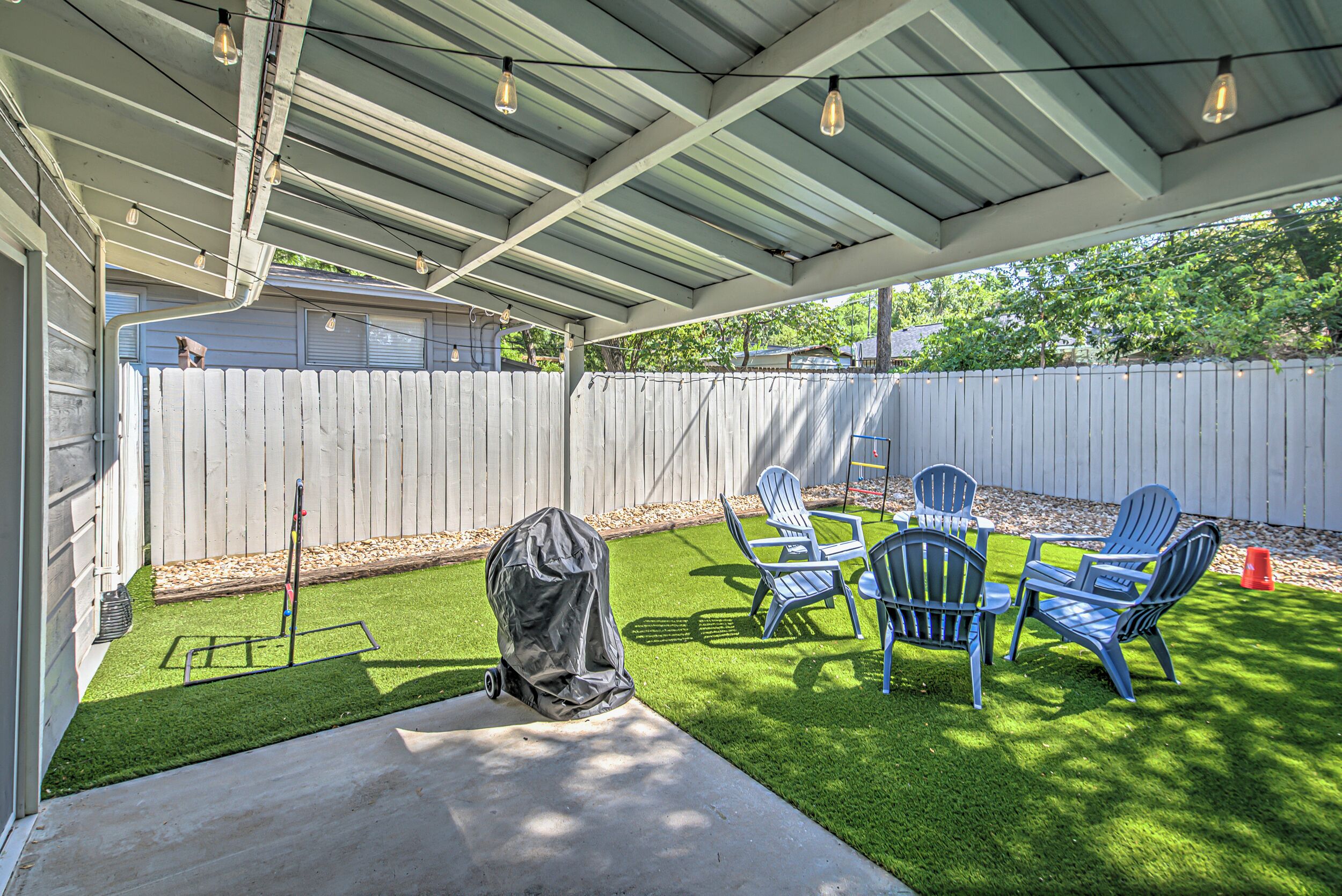 A covered patio with artificial grass, a grill, and outdoor furniture.
