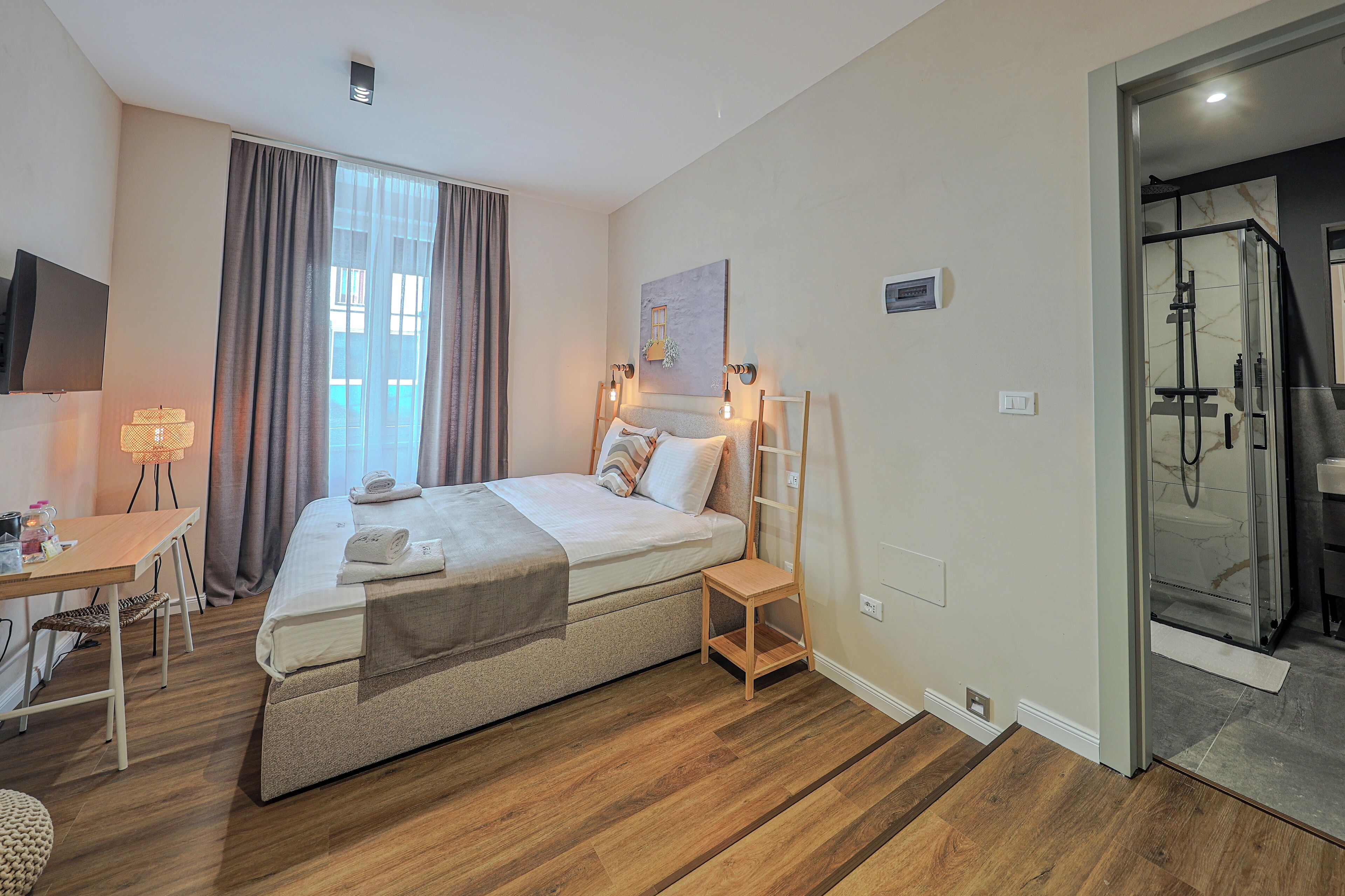 A bedroom with a bed, bedside table, lamp, and a glass shower door.