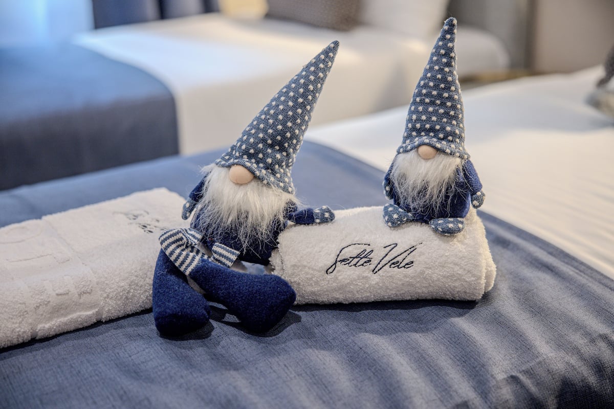 Zwei Gartenzwerge auf einem Bett mit einem weißen Kopfkissen und einer blauen Decke.
