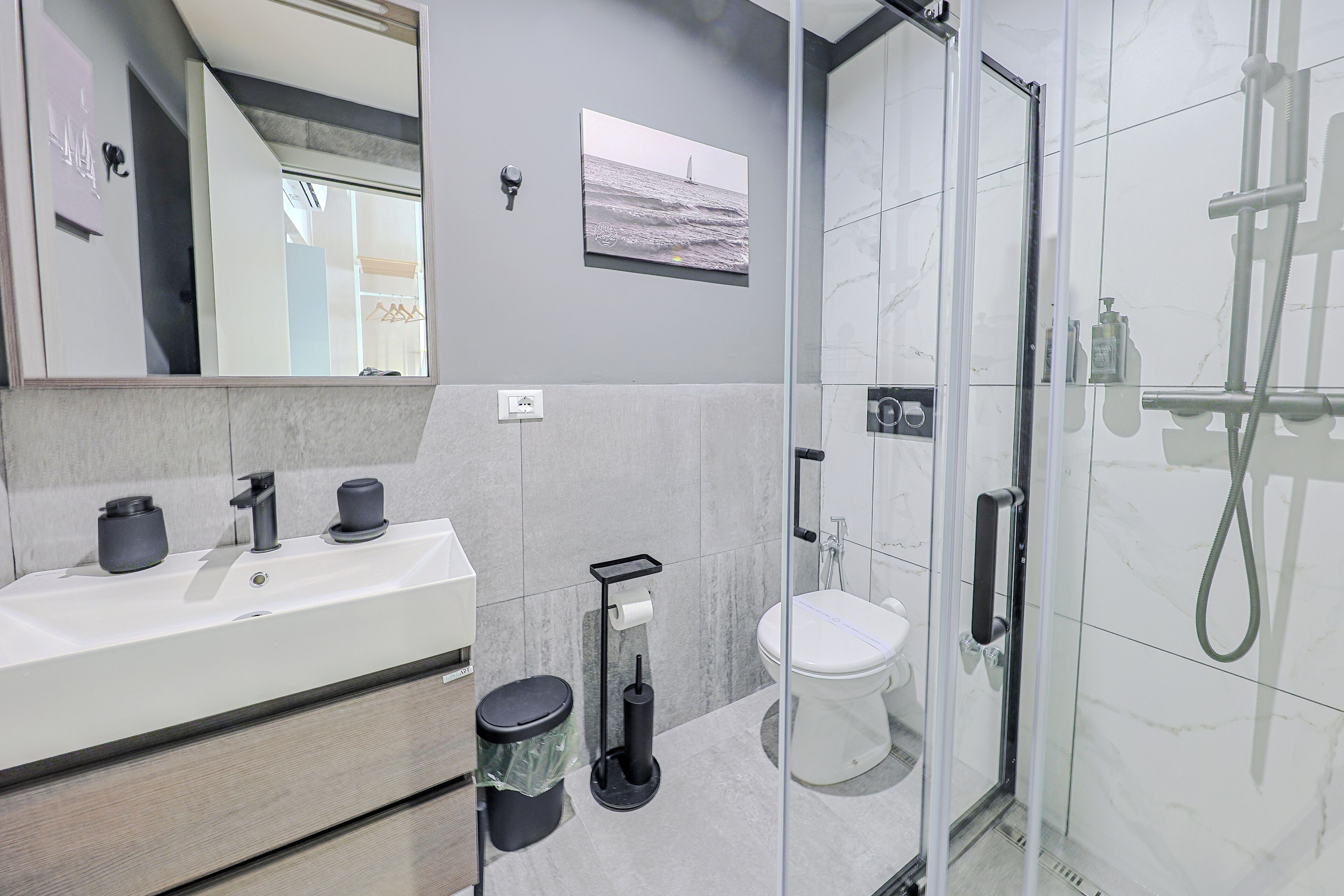 Een moderne badkamer met een douchecabine van glas, een witte wastafel met spiegel en een toilet.