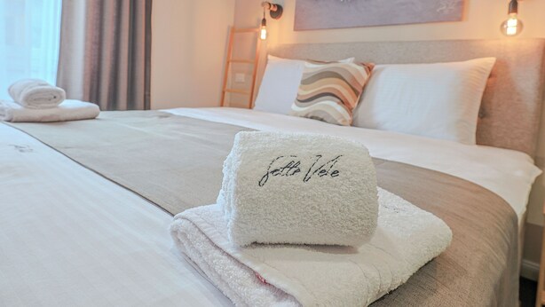 A neatly made bed with a folded towel and a towel with "fête Vélue" embroidered on it. - Sette Vele Rooms  (Trieste)