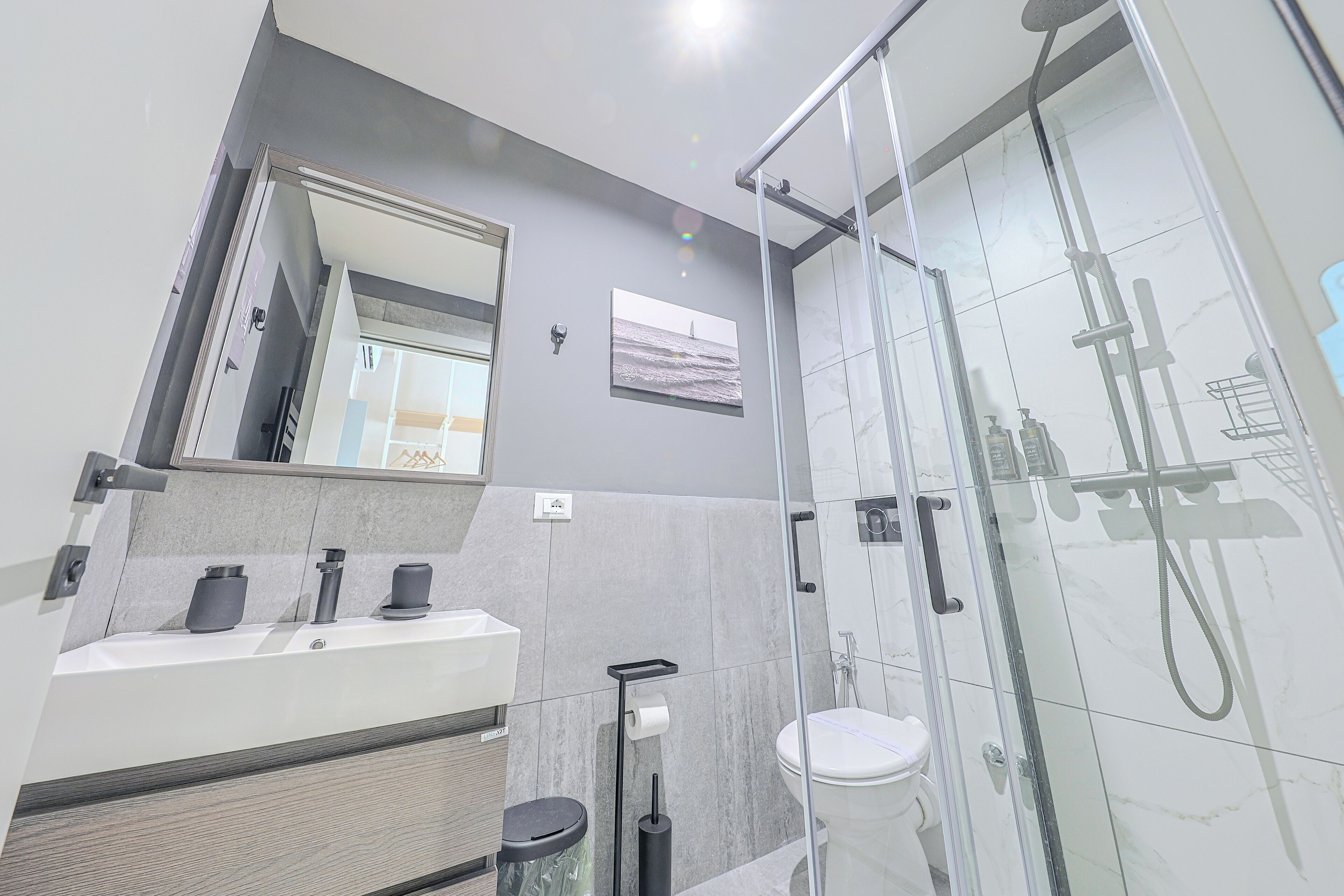 A modern bathroom with a glass shower enclosure, a white sink with a mirror above, and a toilet.