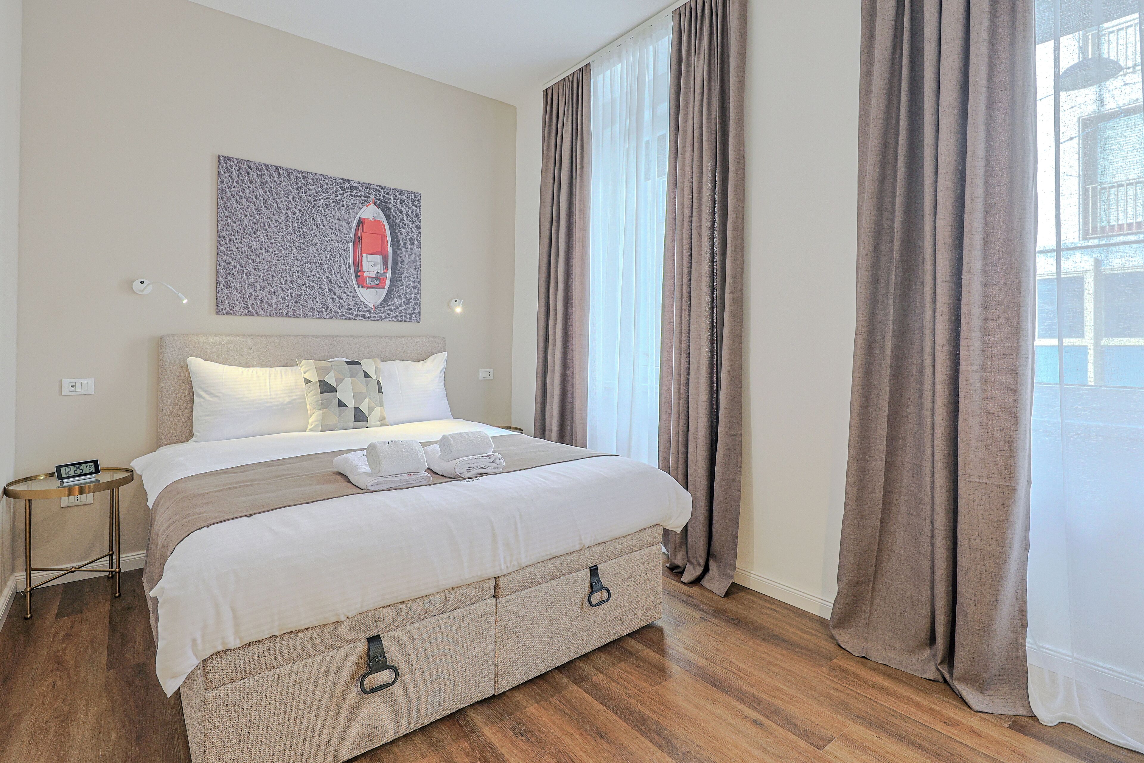 A neatly made bed with a headboard, a bedside table with a lamp, and a wall-mounted artwork.