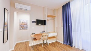 A hotel room with a wooden floor, a desk with a chair, a TV, a wardrobe, and a large window with blue curtains. - Sette Vele Rooms  (Trieste)