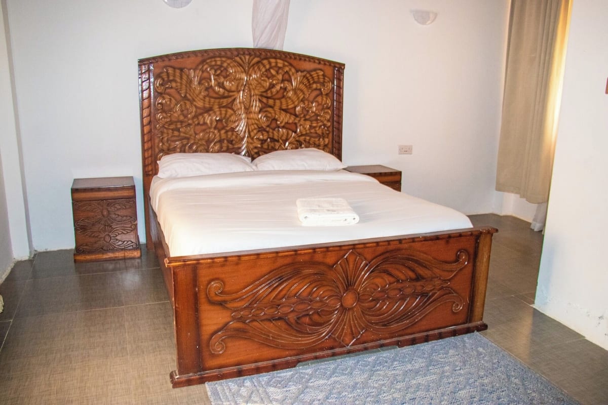 Una cama de madera con cabecera tallada, una mesita de noche y una mesilla.