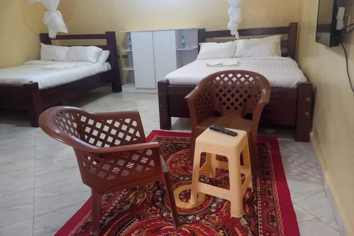 Una habitación con dos camas individuales, una pequeña silla de madera, un taburete y un televisor en la pared.