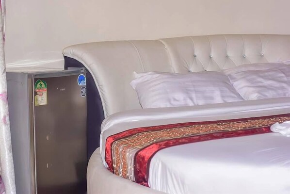 A hotel room with a bed, a small refrigerator, and a wall-mounted control panel. - Falls View Resort Nabuyole (Webuye)