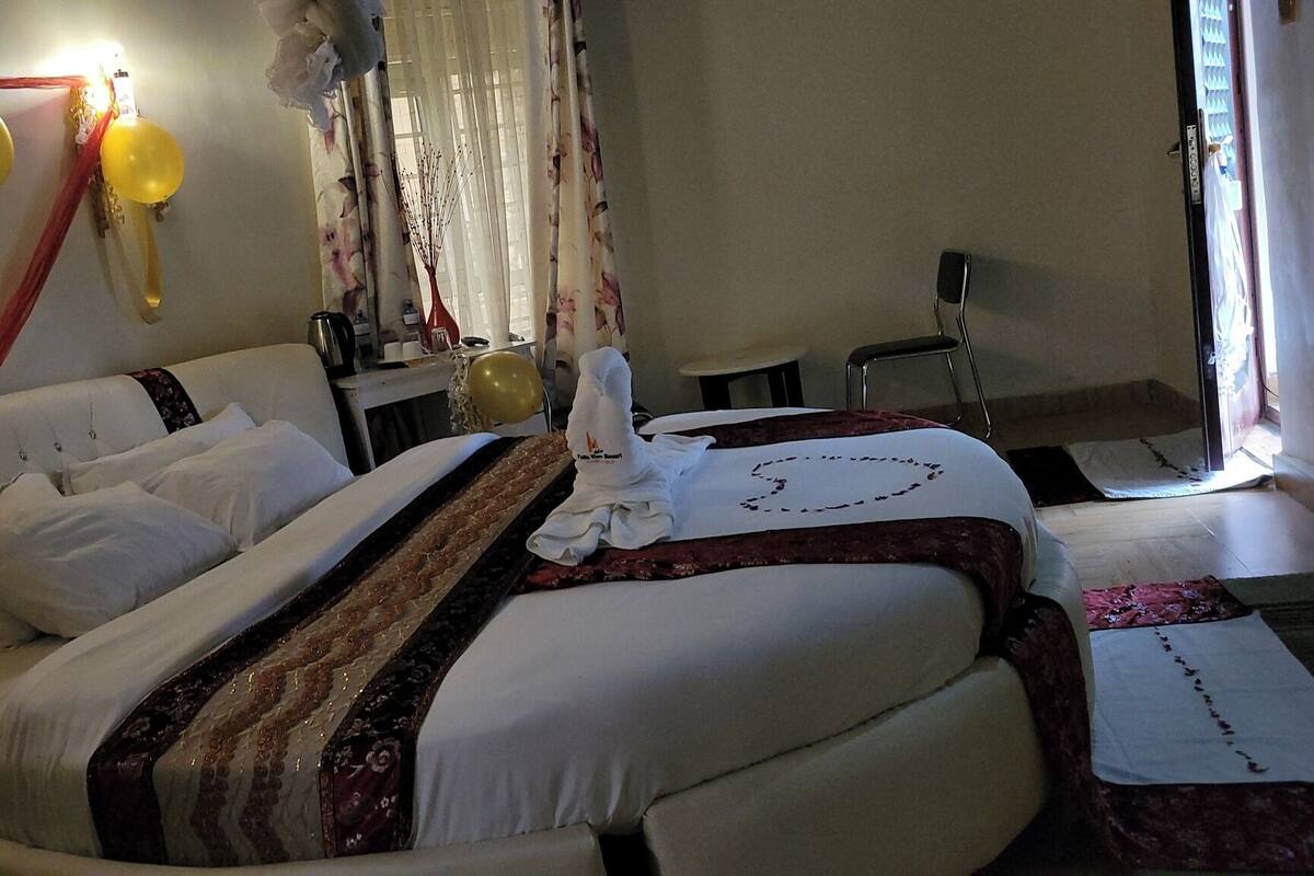 Habitación de hotel con dos camas, un escritorio y una silla. Hay globos en la pared y una ventana con cortinas.