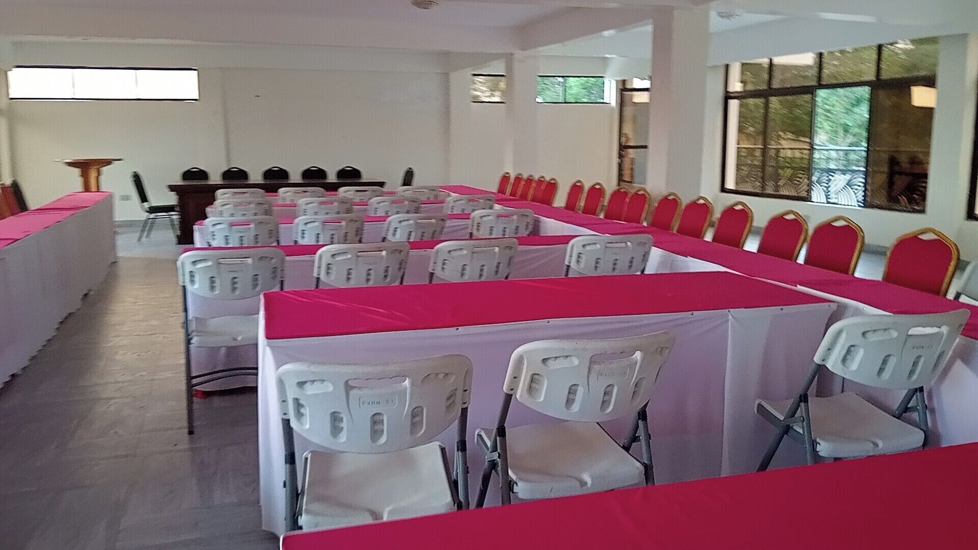 Un salón de conferencias con hileras de sillas blancas y una larga mesa cubierta con un mantel rojo.