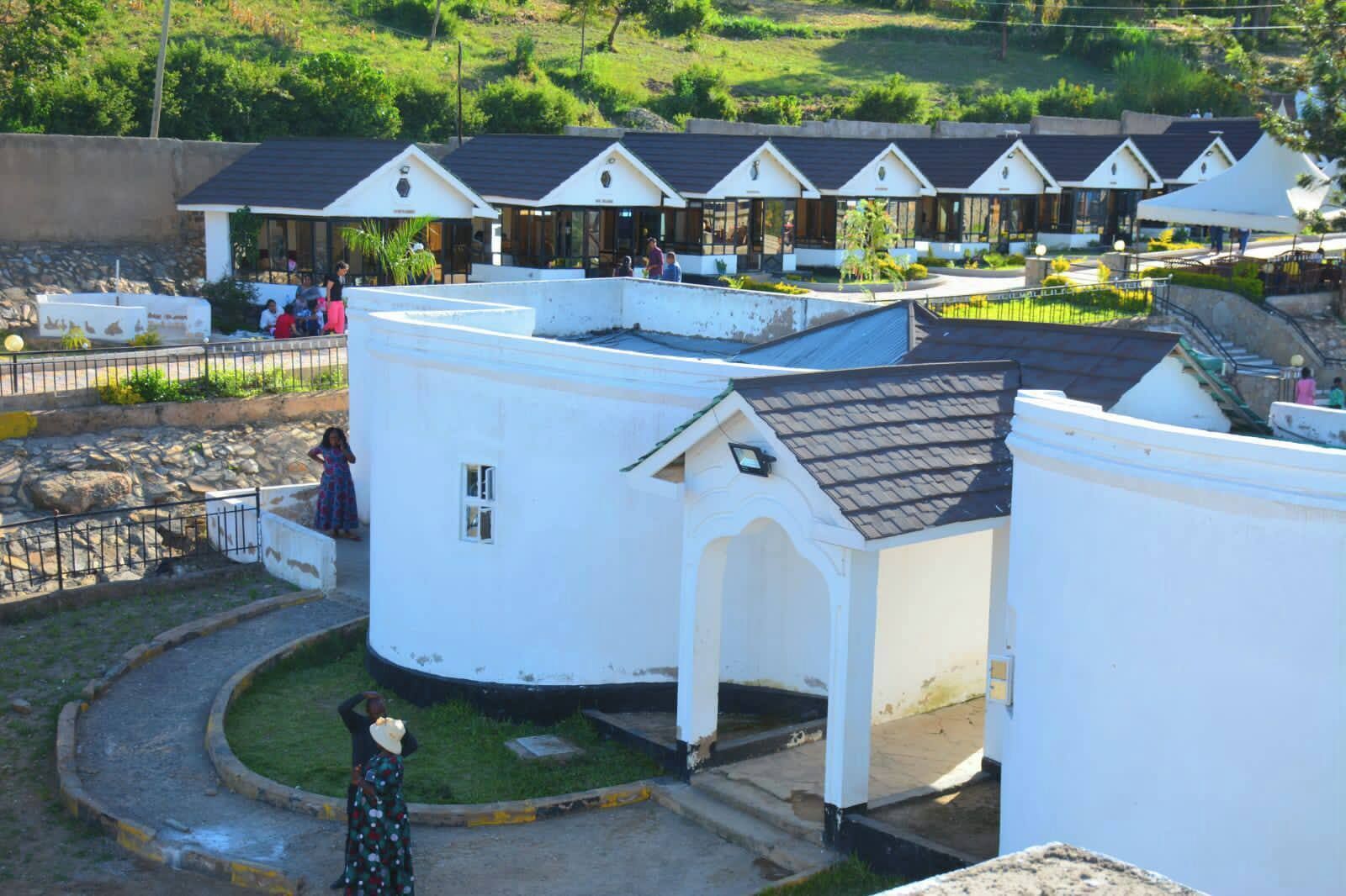 A row of white buildings with pitched roofs, possibly a resort or hotel, with a paved walkway and a grassy area in front.