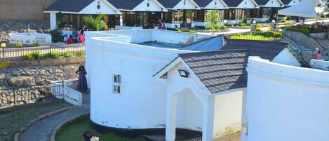 A row of white buildings with pitched roofs, possibly a resort or hotel, with a paved walkway and a grassy area in front.