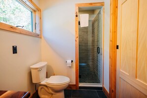A bathroom with a toilet, a glass shower enclosure, and a wooden door. - treehouse in Downeast Acadia Region of Maine (Ellsworth)