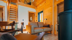 A cozy log cabin interior with a sofa, chairs, a dining table, and a fireplace.