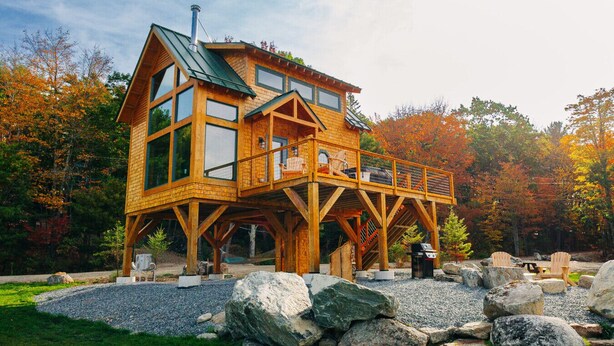 A wooden cabin with a balcony, large windows, and a stone foundation.