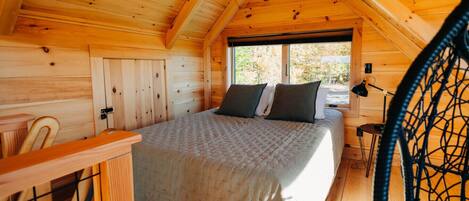 A wooden cabin bedroom with a bed, a chair, and a window.