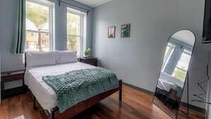 A bedroom with a bed, a nightstand, a mirror, and two windows. - Spacious Modern 7BR Retreat ~ 3 Story Gem in Pittsburgh (Pittsburgh)