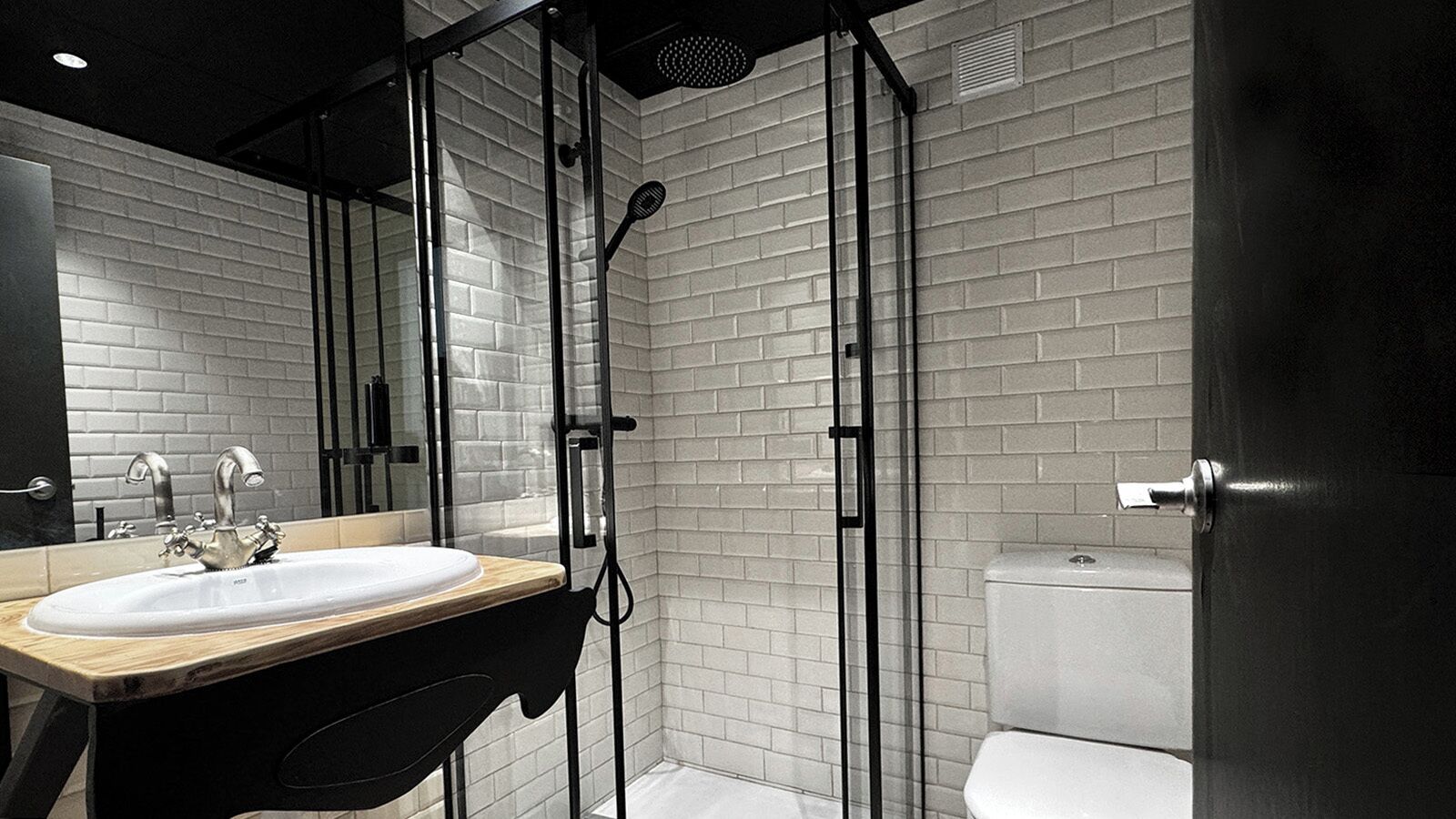 A modern bathroom with a white sink, black countertop, and a glass-enclosed shower area.