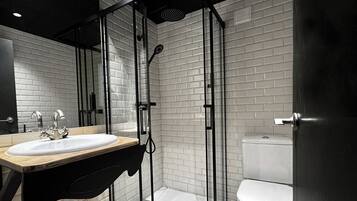 A modern bathroom with a white sink, black countertop, and a glass-enclosed shower area.
