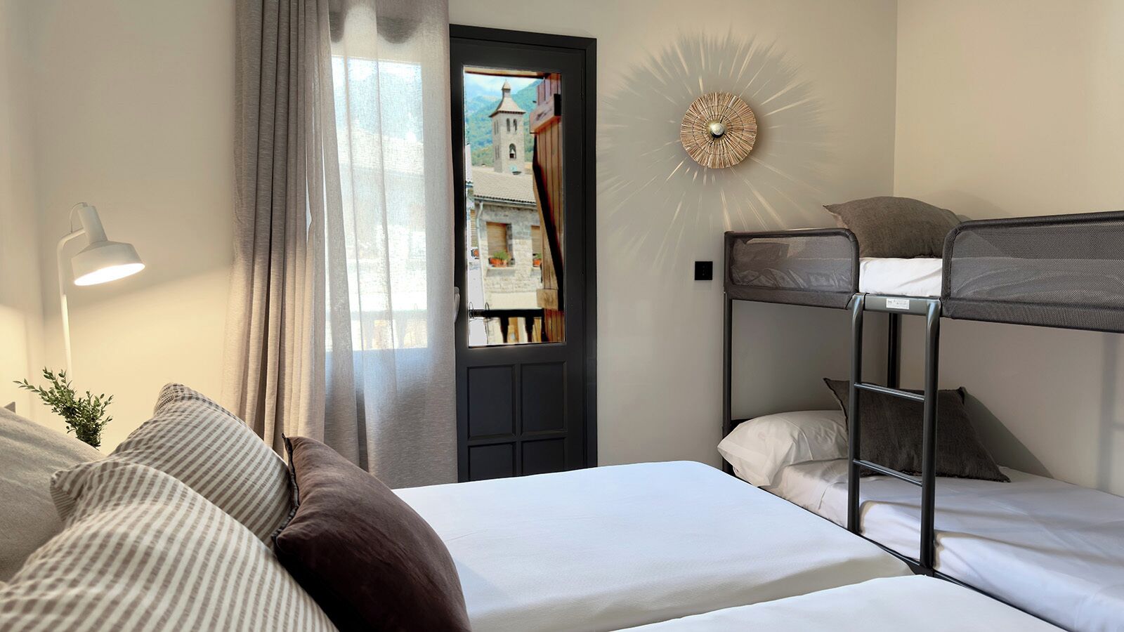 A room with a bunk bed, a desk with a lamp, and a view of a mountain through a window.
