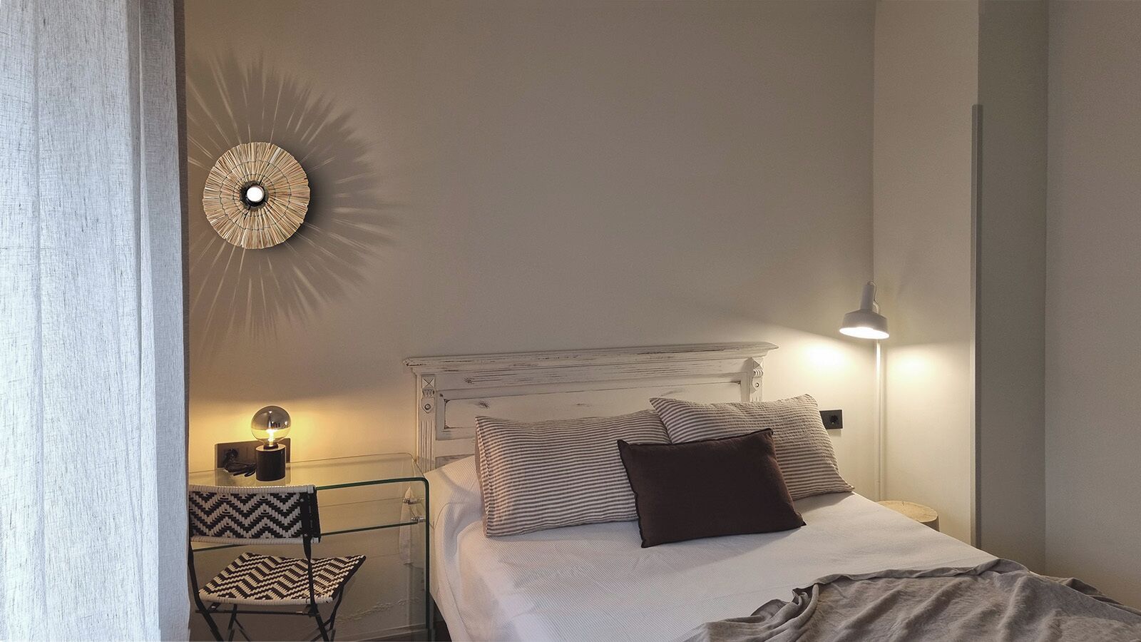 A bedroom with a bed, bedside lamps, a wall clock, and a chair.