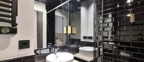 Un baño moderno con un espejo grande, dos lavamanos y una pared de azulejos negros.