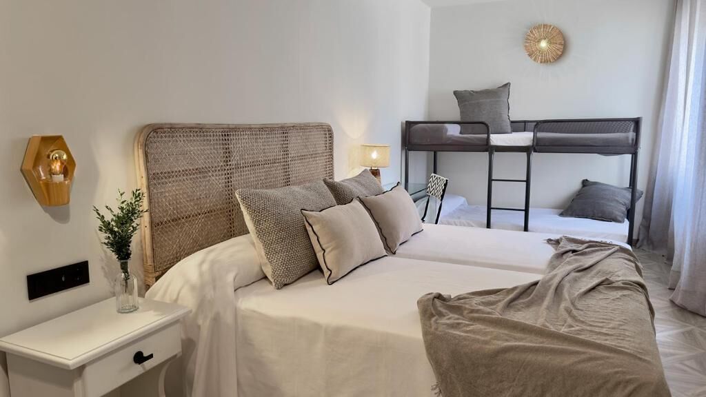A hotel room with a large bed, a desk, and a bunk bed in the background.