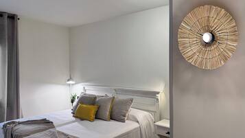 Een net opgemaakt bed met kussens, een nachtkastje en een wandlamp.