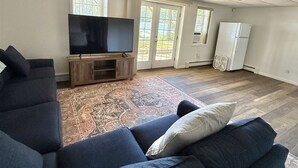 A spacious living room with a large sectional sofa, a flat-screen TV, and a refrigerator. - WATERFRONT ON THOMPSON LAKE (Oxford)