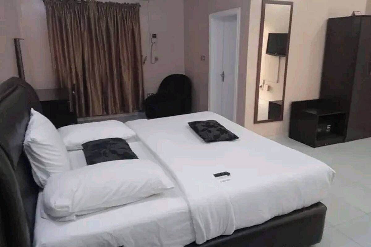 Ein Hotelzimmer mit Bett, Schreibtisch, Stuhl, Klimaanlage, Spiegel und Kleiderschrank.