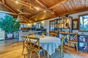 Un intérieur en bois comprenant une table à manger, des chaises, une grande plante en pot et un coin cuisine.