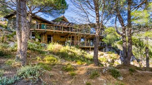 A wooden cabin with a balcony, surrounded by trees and a rocky hillside.