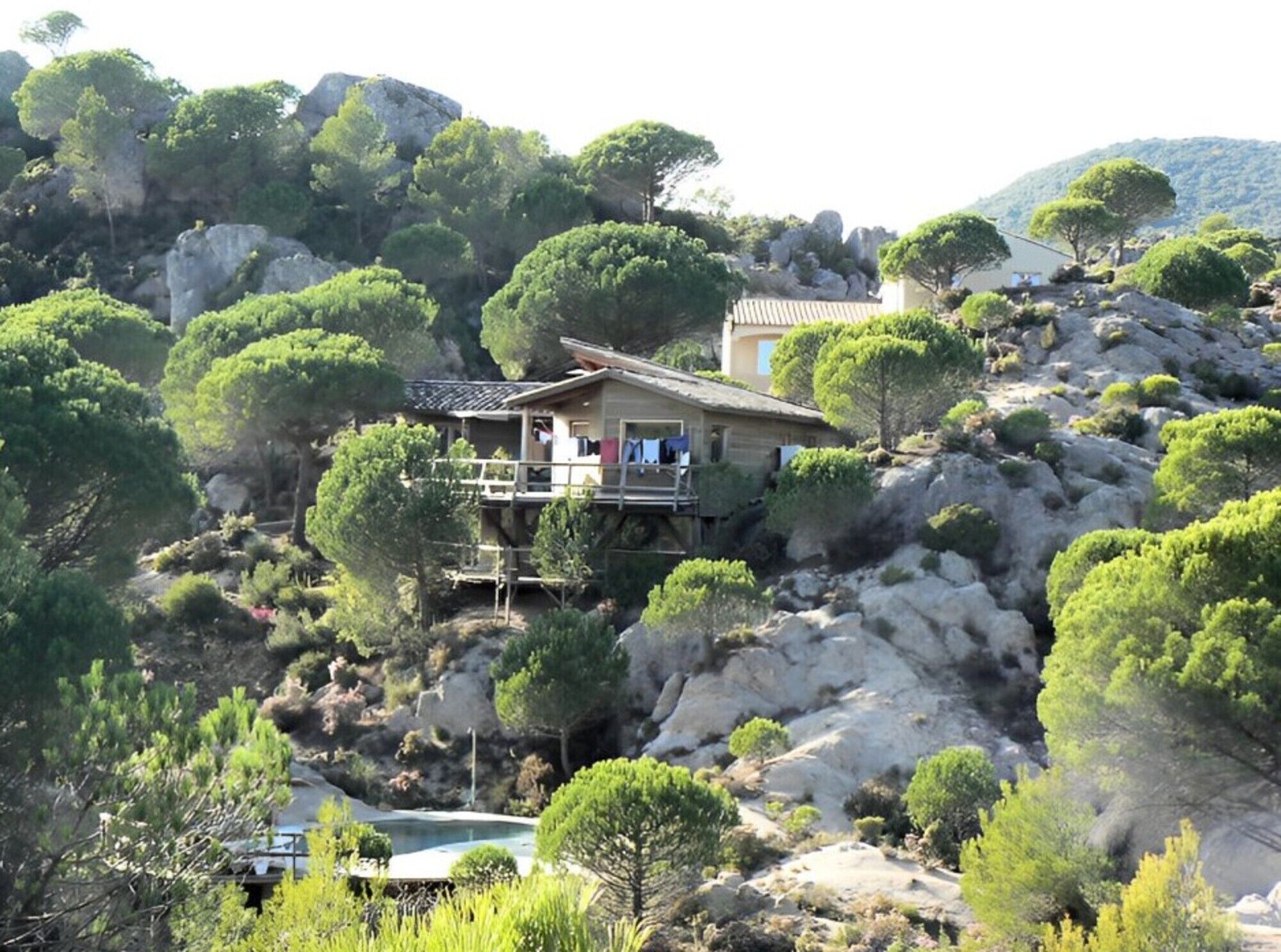 A house with a balcony, surrounded by trees and rocky terrain.