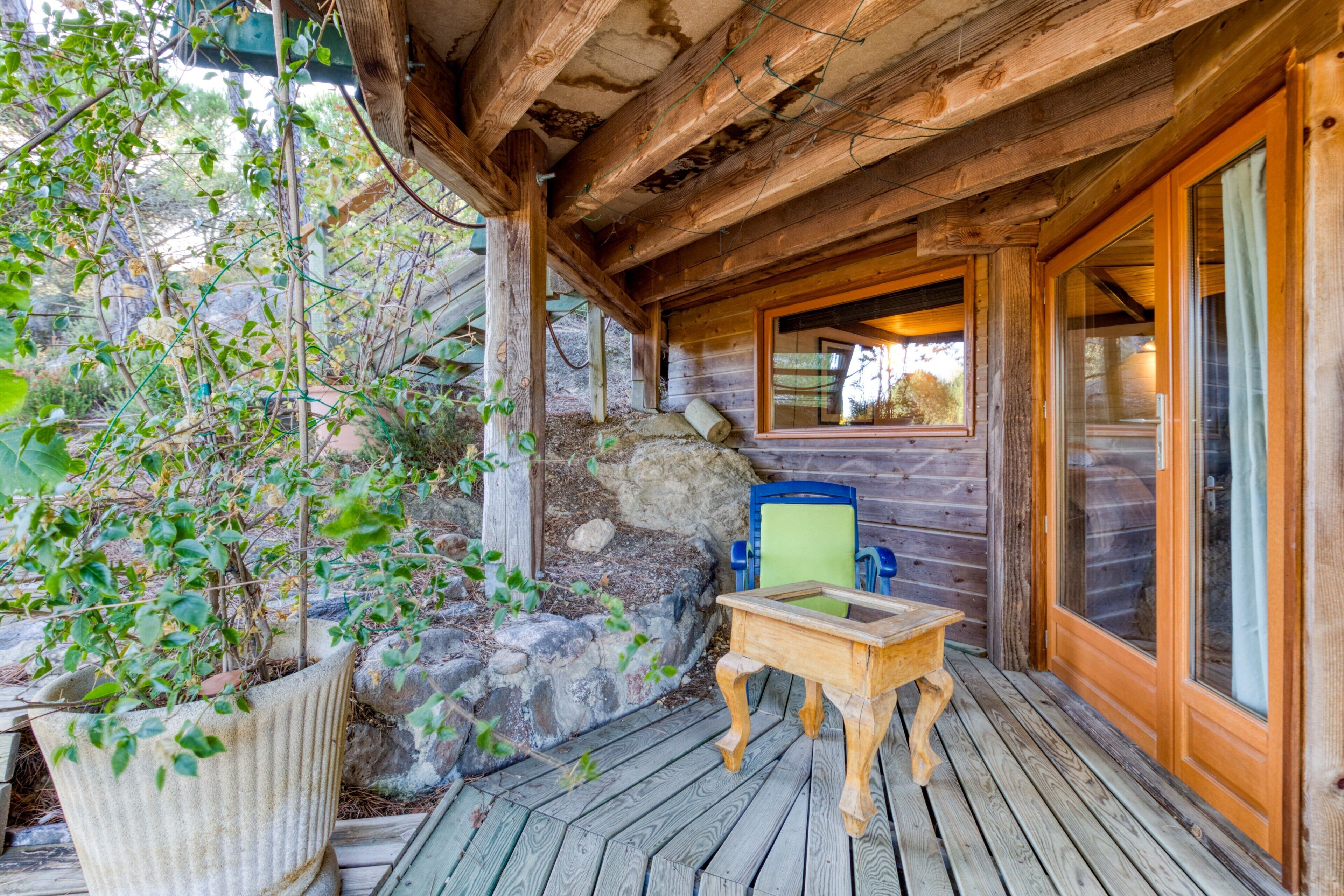 Eine Holzterrasse mit Tisch und Stühlen, eine Steinmauer und ein Fenster.