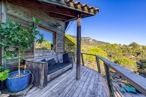 Une terrasse en bois avec un canapé intégré, une grande plante en pot et une vue sur un paysage montagneux.